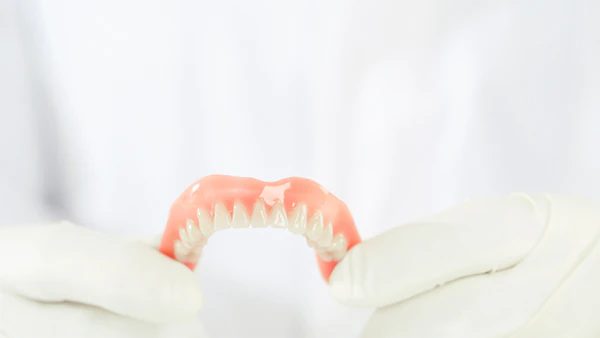 Gloved hands holding a complete denture